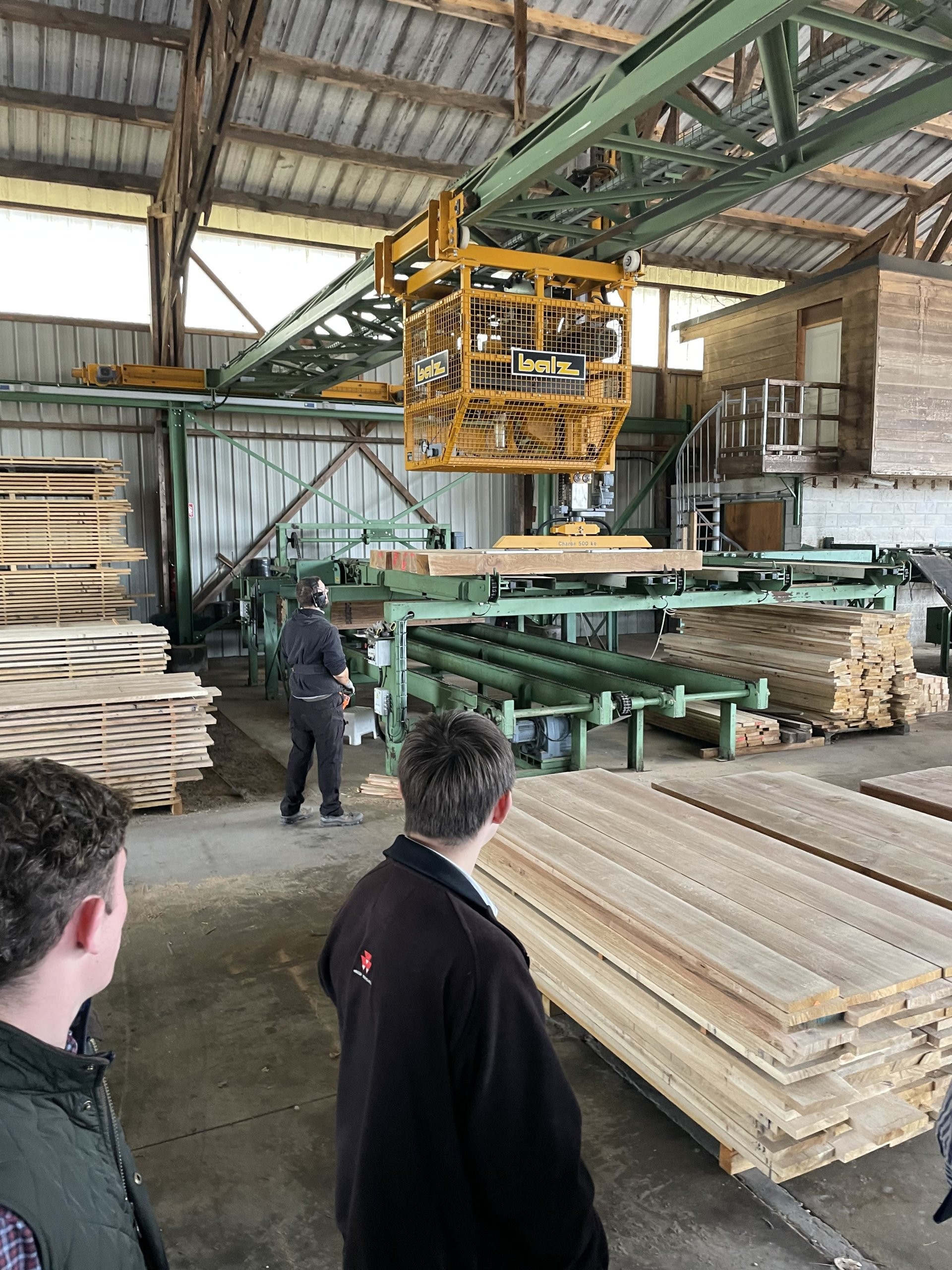 Visite d’une scierie, entre les machines de production et les piles de planches.