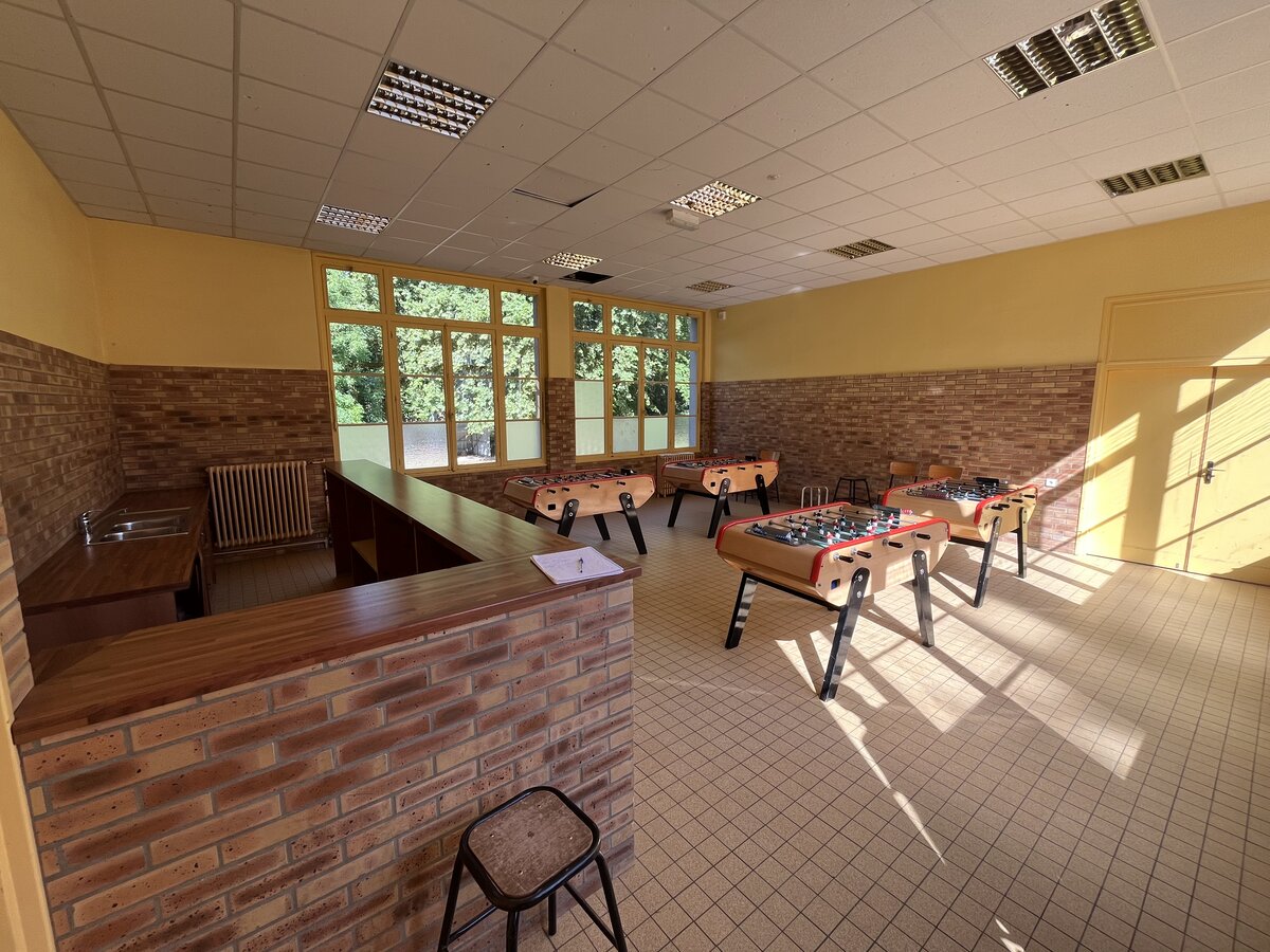 Salle commune de l'internat avec bar en briques et tables de baby-foot